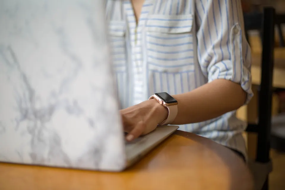 A wrist wearing a smartwatch next to a laptop